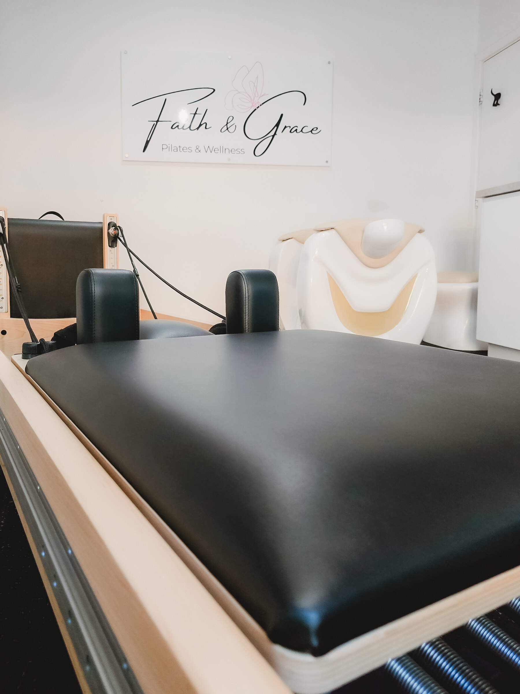 Reformer bed beneath the Faith & Grace Pilates & Wellness studio sign